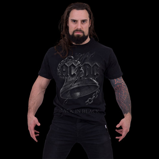 A man with long dark hair and a beard stands with arms slightly out, wearing the Spiral USA AC/DC "Back In Black" Torn Shirt and black jeans against a solid black background. A tattoo sleeve is visible on one arm.