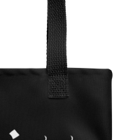 Close-up of the upper corner of the Decaying Eucharist "Logo" Tote Bag by Mainstay Entertainment, showing a textured black strap, visible stitching, and a partial white geometric logo at the bottom left for stylish detail.