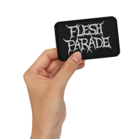 A hand holds the Mainstay Entertainment Flesh Parade "Classic Logo" embroidered patch—black, rectangular, with jagged white text—against a plain white background.