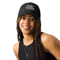 A smiling woman with long braids wears a black tank top and the Flesh Parade "Embroidered Logo" Under Armour® Hat, featuring white lettering, against a plain light background.