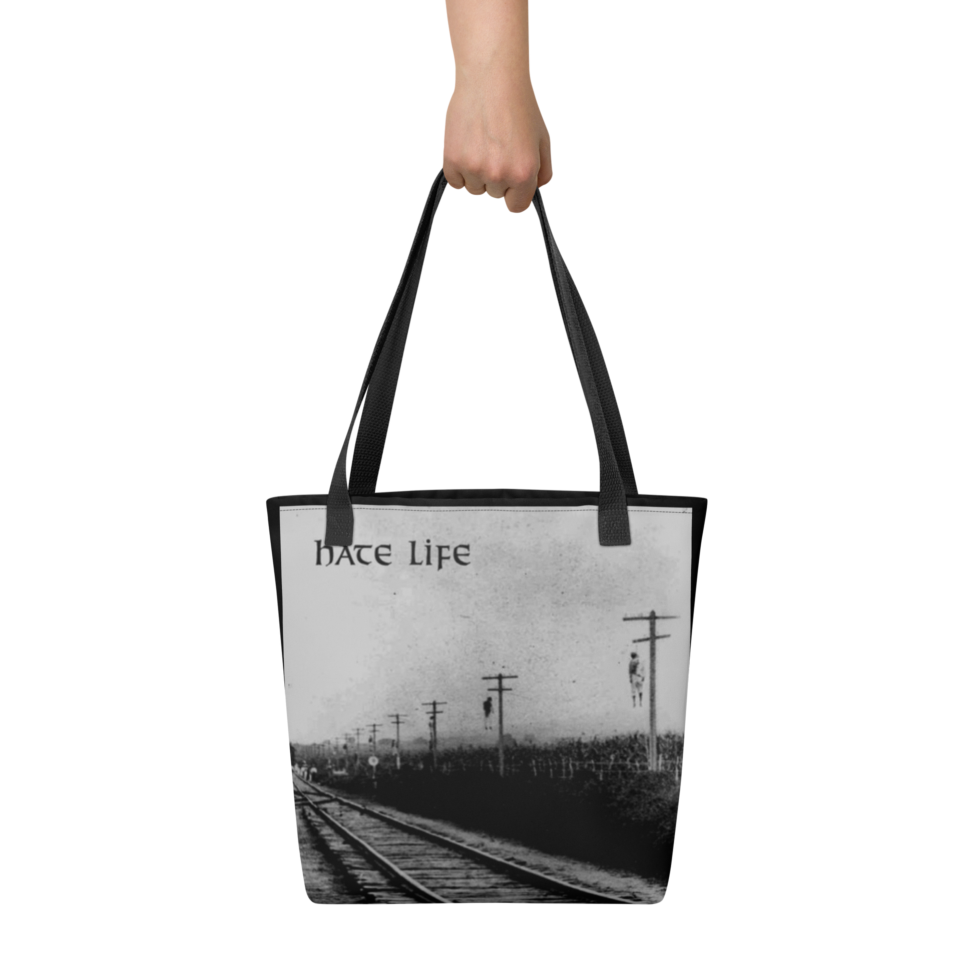 A hand holds the Flesh Parade "Hate Life" Tote Bag by Mainstay Entertainment, featuring railroad tracks with telephone poles and "hate Life" printed at the top left in black and white.