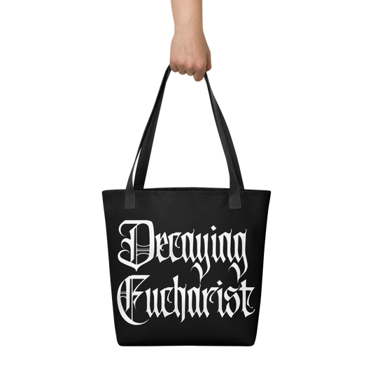 A hand holds the Decaying Eucharist "Logo" Tote Bag by Mainstay Entertainment, featuring large white gothic lettering.