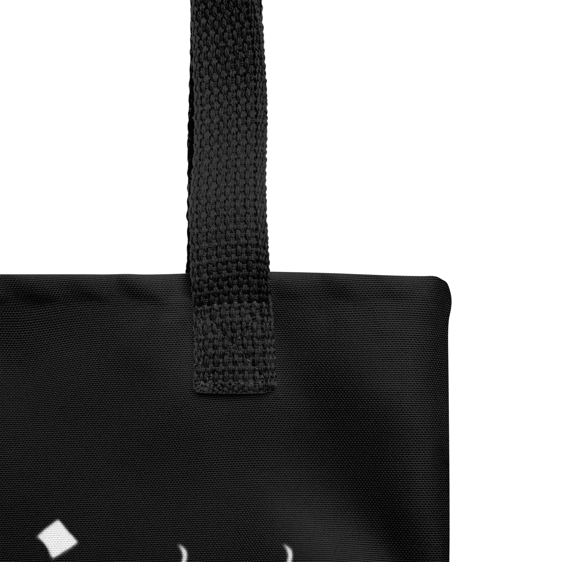 Close-up of the upper corner of the Decaying Eucharist "Logo" Tote Bag by Mainstay Entertainment, showing a textured black strap, visible stitching, and a partial white geometric logo at the bottom left for stylish detail.
