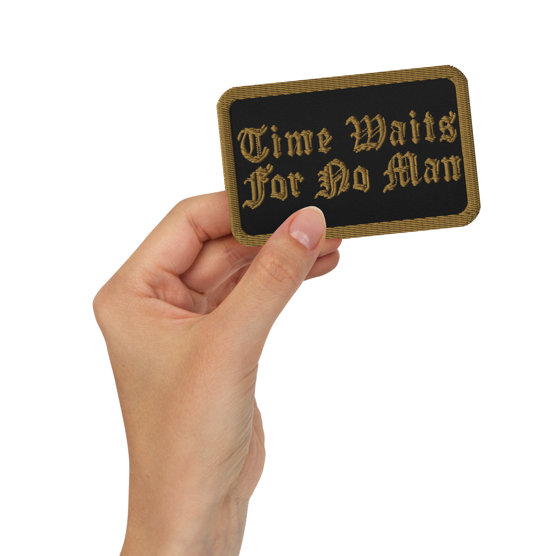 A hand holds the Mainstay Entertainment Time Waits For No Man "Logo" Embroidered Patch—rectangular, black, with gold trim and ornate text reading “Time Waits For No Man.”.