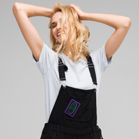 A smiling person with blonde hair, in a white tee and black overalls, stands with hands in their hair. The SHRÜM 