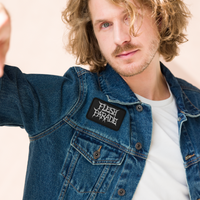 A man with wavy, shoulder-length blond hair wears a denim jacket featuring the Mainstay Entertainment Flesh Parade 