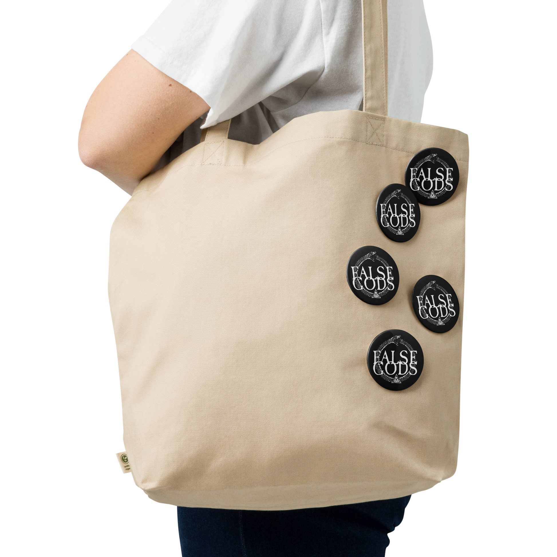 A person in a white shirt carries a beige tote bag adorned with Mainstay Entertainment's False Gods "Snake Logo" Set of 5 glossy buttons. The background is plain white.