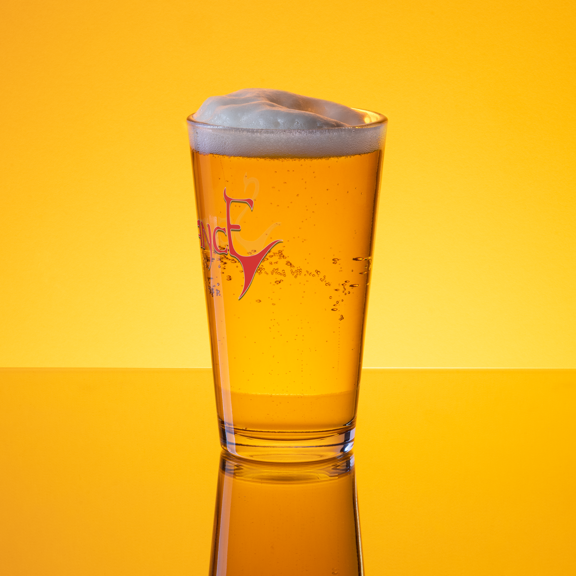A Severance "Logo" Pint Glass by Mainstay Entertainment filled with golden beer and a foamy head, set against a vibrant yellow background with reflections beneath the glass.