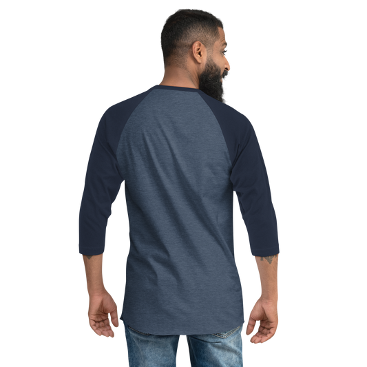A bearded man is seen from behind wearing a Mainstay Entertainment Noz Redna "Candle Logo" 3/4 Sleeve Raglan Shirt and blue jeans, standing against a plain light background.